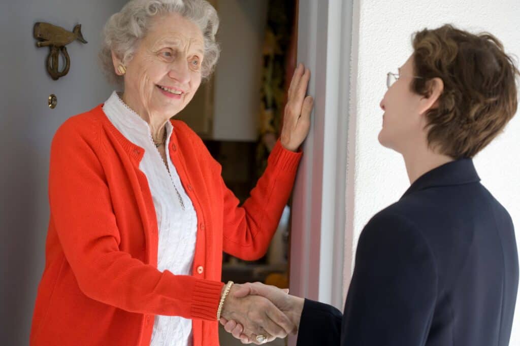 A senior lady at the front door greeting a neighbour