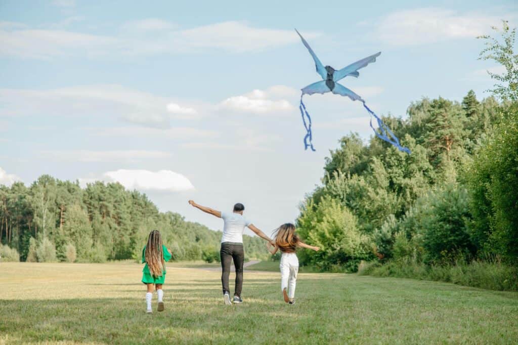 A father with daughters playing kite in the park.