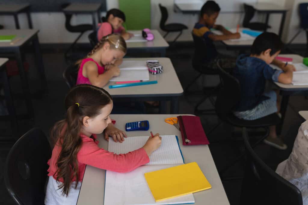 Side view of kids studying and sitting at desk in classroom in school