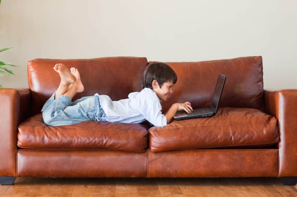 A kid playing with a laptop on the sofa