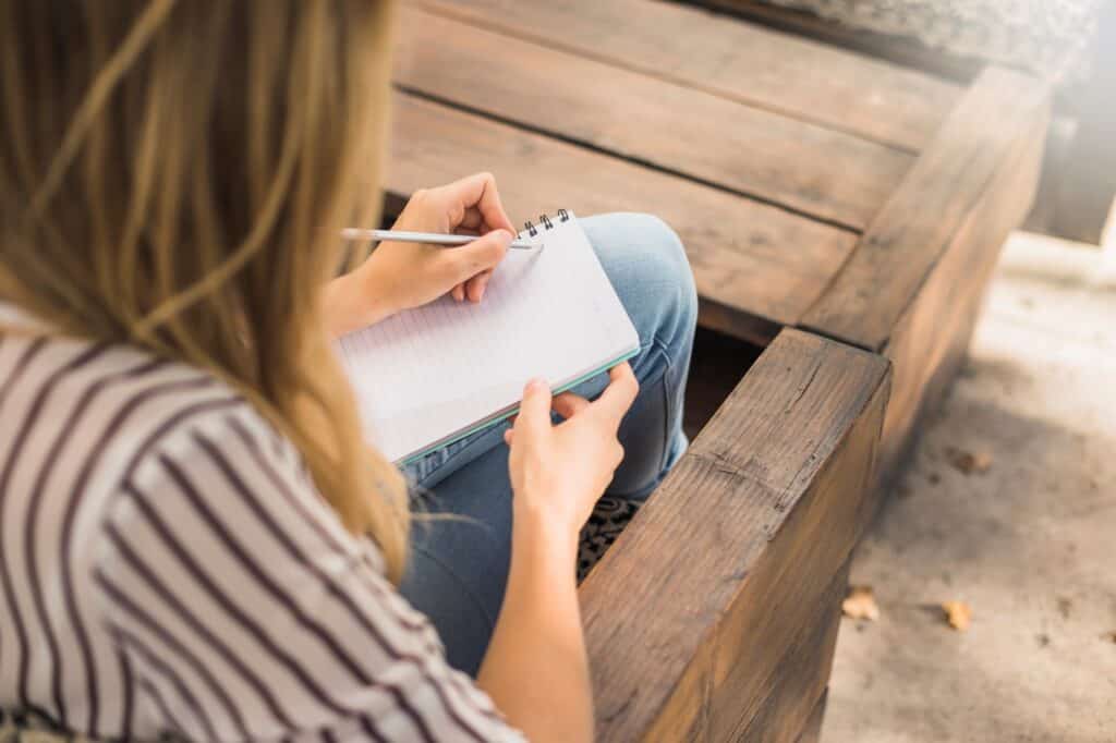 A woman with a notebook and pencil while sitting on a bench in the concept of 'How to Create a Moving Checklist for Your Move to Croydon'.